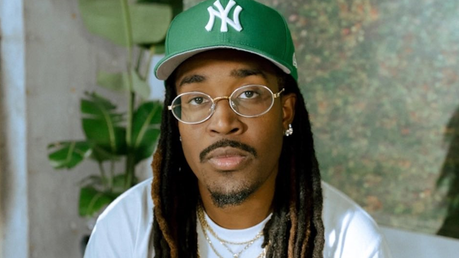 Young black man wearing light golden frames and a green Yankees cap.