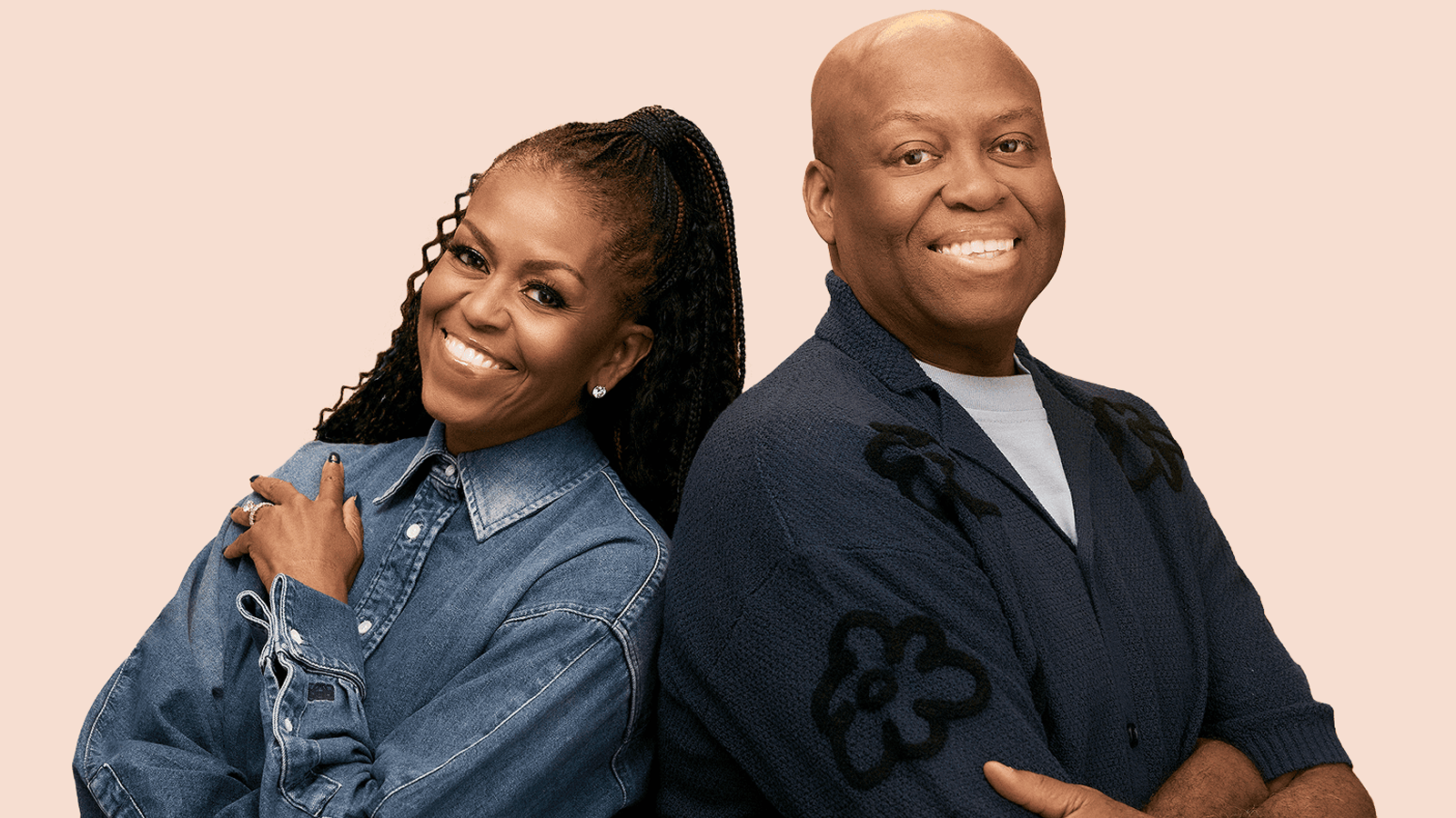 Michelle Obama (left) and her big brother Craig Robinson (right) leaning on each other's back facing the camera with smiling confident expressions