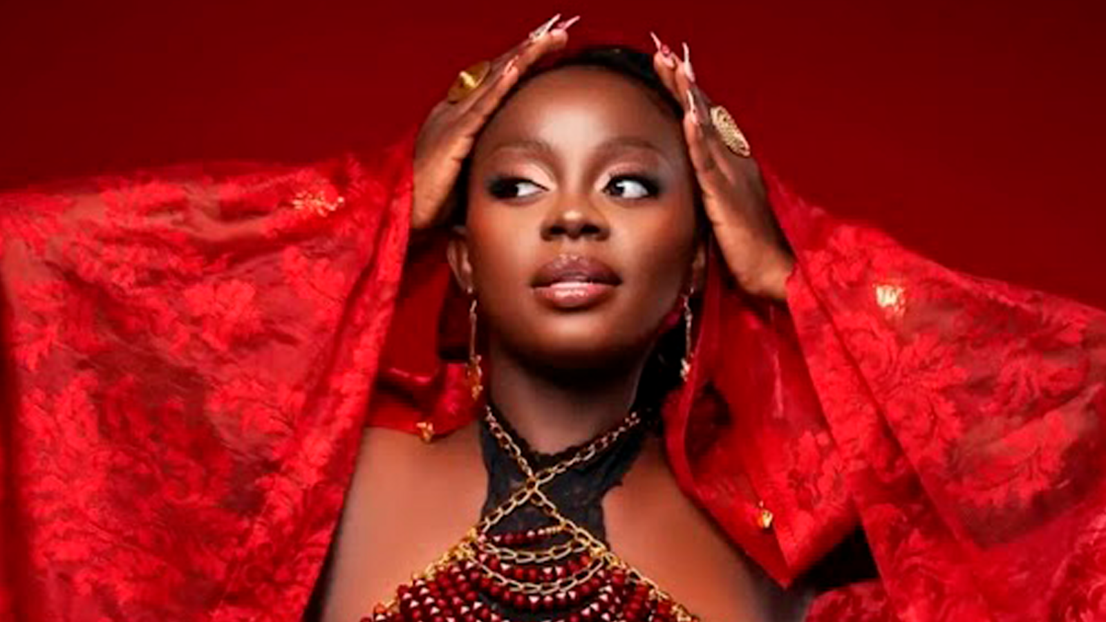 Black young Kenyan singer artist Hildah Watiri wearing a vibrant red dress holds her hair with both hands while looking to the side.