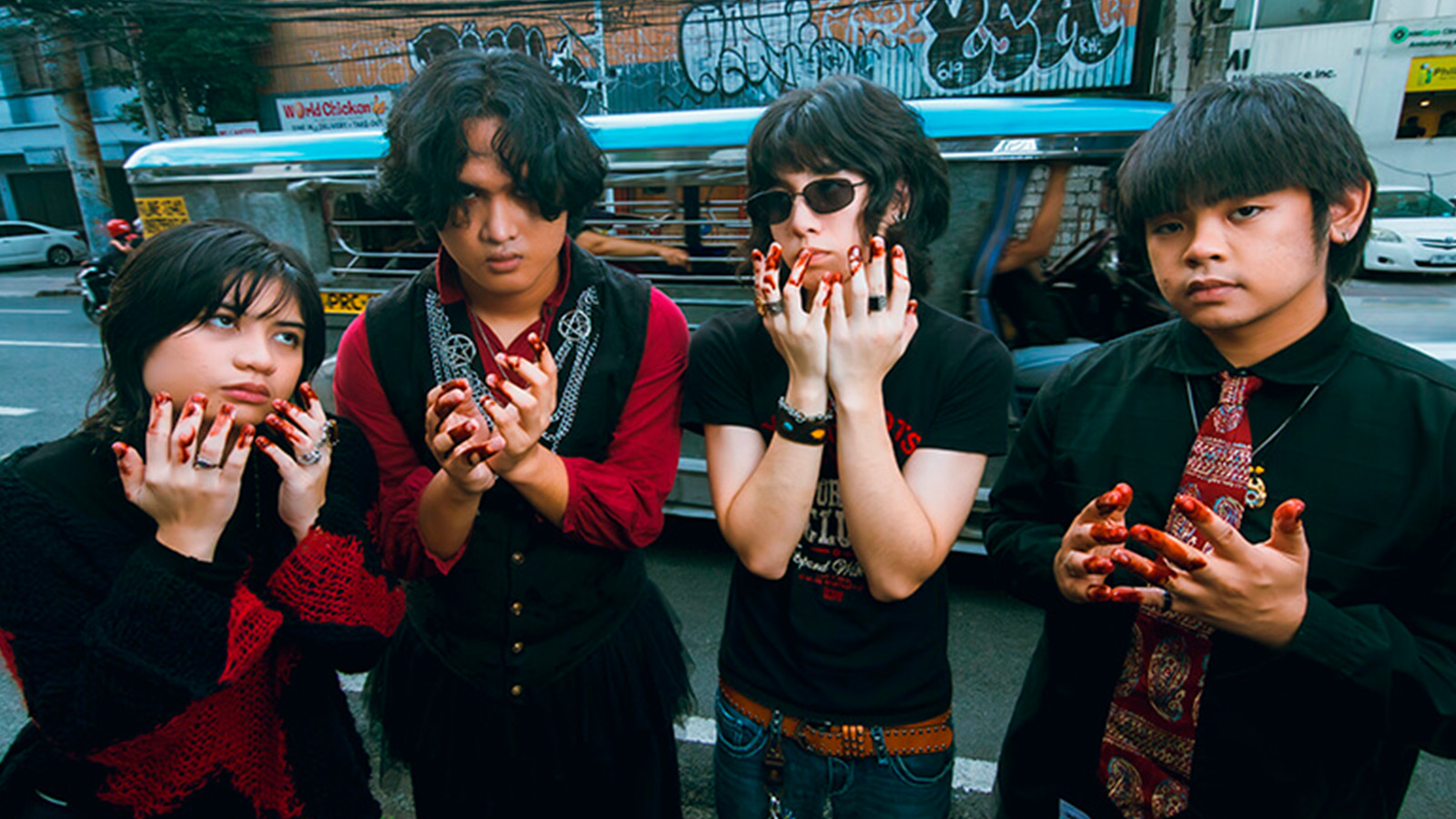 fitterkarma members standing at the pavement with a car passing in the back and hands covered in blood like substance. From left to right: Sophia Miranda (bass, vocals), Joao de Leon (vocals), Lory Mendoza (lead guitar, backup vocals), and Sanders Bayas (drums).